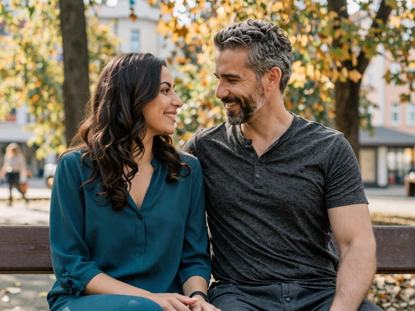 James and Amira, an American-Bosnian couple, sitting together in a Sarajevo park surrounded by autumn leaves